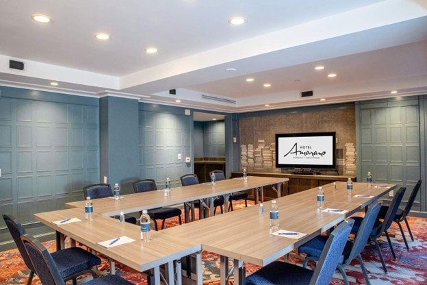 Meeting room at Hotel Amarano in Burbank with U-shaped tables, chairs, and a presentation screen.