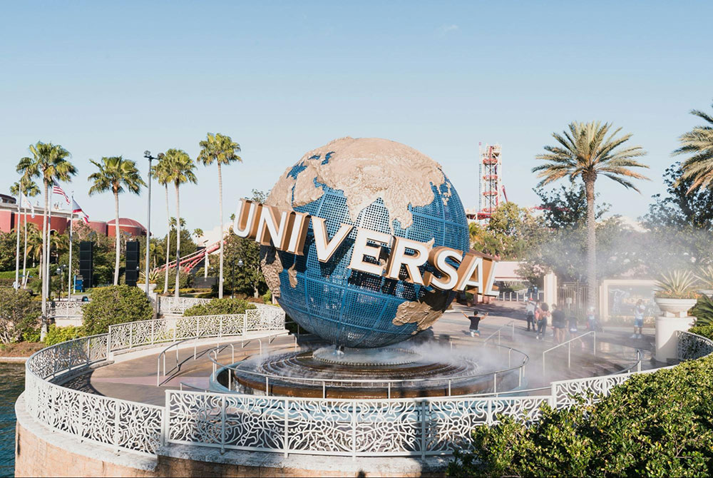 Universal Studios globe fountain surrounded by palm trees and landscaped walkways on a sunny day.